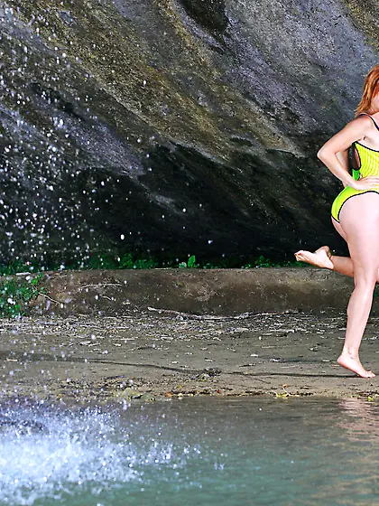 Redhead takes off her onesie to pose naked under a waterfall Vid