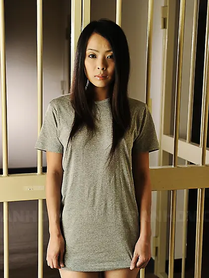 Oriental inmate girl demonstrates small breasts by the bars of t