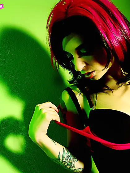 Joanna Angel strips in front of a green wall